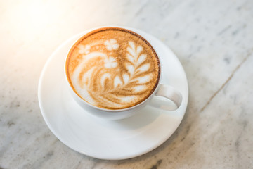 Two cups of coffee with beautiful leaf and pig latte art and sun flare lighting on a marble table in a coffee shop in the morning.