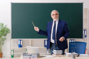 Aged male teacher in front of chalkboard 