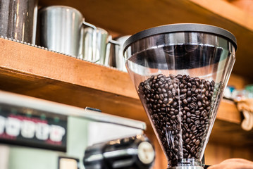 Coffee beans in electric coffee grinder with coffee shelf background in the coffee shop.
