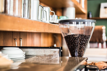 Coffee beans in electric coffee grinder with coffee shelf background in the coffee shop.