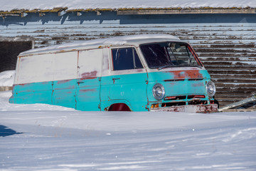 Abandoned vintage 1960’s blue and white van rusting in the snow of a Saskatchewan farmyard