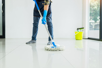 Young housekeeper cleaning floor mobbing holding mop and plastic bucket with brushes, gloves and...