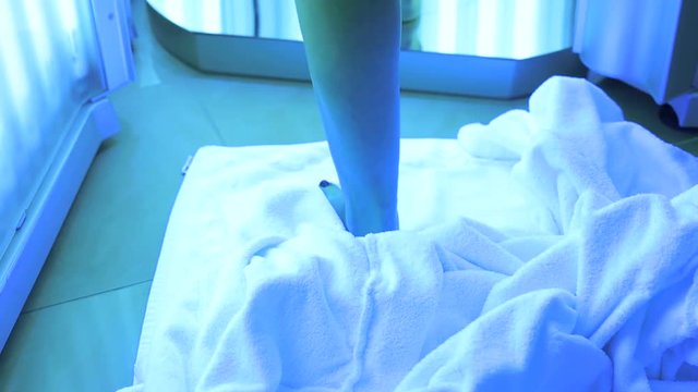 Close-up of bare feet girl who stands in the Solarium and sunbathes. The girl takes off her white robe and throws it on the floor under her feet. Medical tanning procedure.