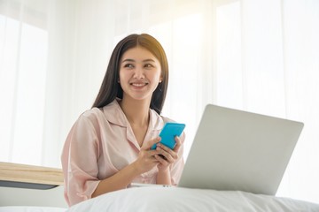 Portrait of smiling beautiful lady wake up viewing mobile phone and working with notebook on the bed with copy space