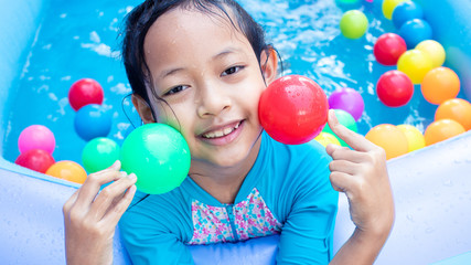 Fototapeta na wymiar Asian Child Girl Having Fun In Garden Paddling Pool with color ball