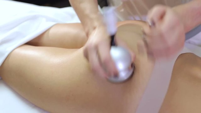 Close-up of a woman masseur doing a vacuum massage of the buttocks for a young woman. Cosmetology, body and skin care. Vacuum roller massage with the possibility of ultrasonic action.