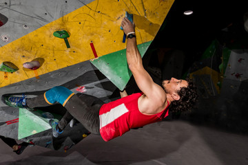 Obraz premium Rock climber man hanging on a bouldering climbing wall, inside on colored hooks