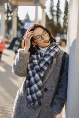 Fototapeta premium Attractive young girl wearing glasses in a coat walking on a sunny day