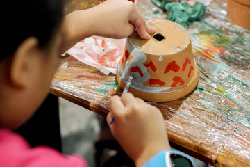 Asian little girl study and learning paint on flower pot in the art classroom of her school.