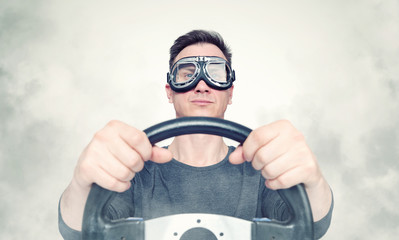 Confident man in stylish goggles with steering wheel, smoke around. Front view. Car driver concept 
