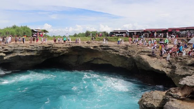 Tourist close to the edge of Devil's Tear watching the waves and mist spray up in Nusa Lembongan, Indonesia