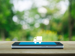 Truck delivery flat icon on modern smart mobile phone screen on wooden table over blur green tree...
