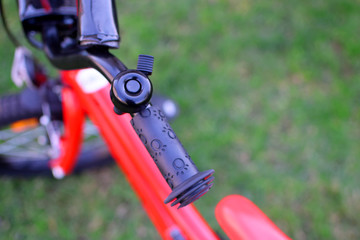 Black bicycle bell ring for safety on handle on green blurred grass and red children bike background with copy space. Part of sport activity equipment for kids.
