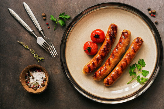 Grilled sausages with tomatoes and spices in a plate on a brown rustic background. Top view, flat lay.
