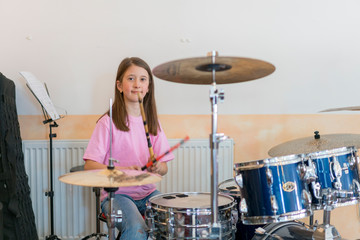 Fototapeta na wymiar Little caucasian girl drummer playing the elettronic drum kit and shuoting. Teen girls are having fun playing drum sets in music class. Close-up photo.