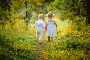 Two children a boy and a girl walk along the path barefoot holding hands