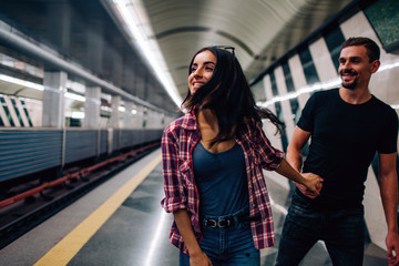 Young man and woman use underground. Couple in subway. Cheerful picture of young woman with man. He hold her hand and follow model. Love story. Underground action.