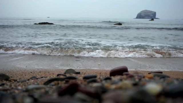  Big waves crashing against a golden sandy beach with Bass Rock producly sitting in the background. 4K VIDEO 