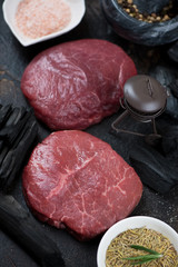 Pair of raw fresh marbled beef steaks with decorative grill and charcoal ready to be cooked, close-up
