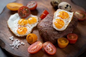 Grilled marbled beefsteak with fried quail eggs and cherry tomatoes, close-up, selective focus