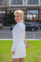 Luxurious woman in white jacket and skirt at city street . Lady with bright makeup and red lips in European streets 