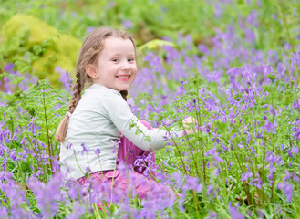 Young girl happy laughing picking bluebell flowers outside in spring summer forest woodland