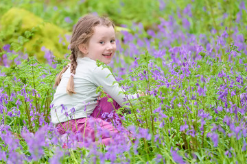 Young girl happy laughing picking bluebell flowers outside in spring summer forest woodland