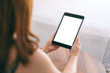 Mockup image of a woman holding and using tablet pc with blank screen while sitting beside the bed