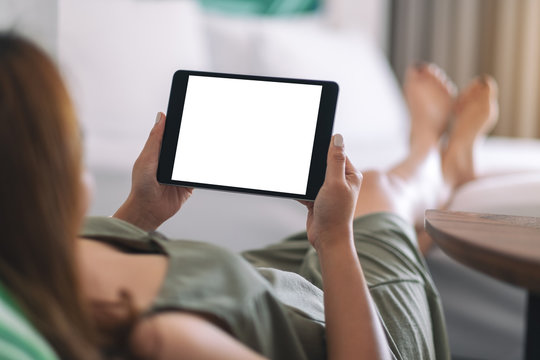 Mockup image of a woman holding and using tablet pc with blank screen while relaxing and lying on the bed