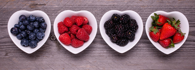 in the four white ceramic heart-shaped bowls, ripe berries, in the foreground, on the rough wooden...