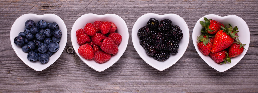 in the four white ceramic heart-shaped bowls, ripe berries, in the foreground, on the rough wooden table