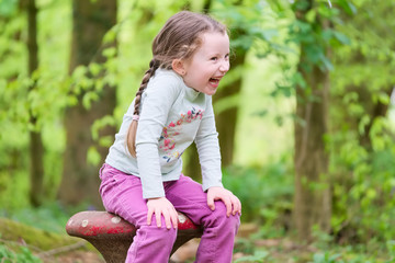 Young girl sitting laughing hands on knees in woodland forest