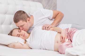 Happy couple waking up in the morning  at home. Husband kissing his sleeping pregnant wife
