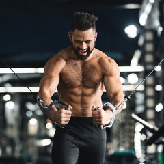 Fototapeta na wymiar Strong muscular man training with block exerciser in gym