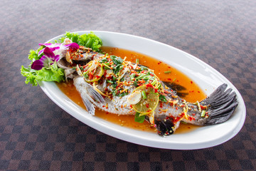 Steamed sea bass fish with lemon put a white ceramic dish on leather floor the grid pattern.
