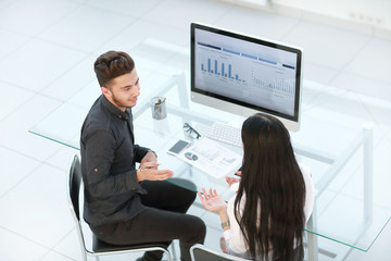 two employees discuss financial data sitting at an office Desk