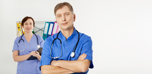 Male doctor with crossed arms and female doctor with folder in medical office, medical insurance, copy space, selective focus.