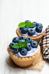 Mini tarts with blue cream and fresh blueberries on white wooden table
