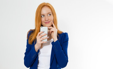 Pretty redhead girl with phone smiling isolated on white background. Young foxy female in business outfit, has amazed look, indicates with fore finger at right upper corner, shows.