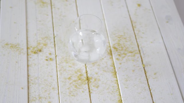 Glass with crystal water and ice cubes on white table with sand