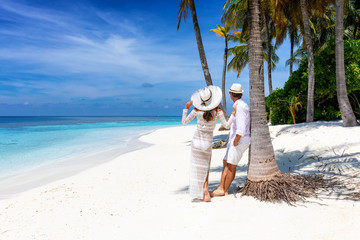 Glückliches Paar steht an einem tropischen Strand unter Palmen und genießt den Urlaub