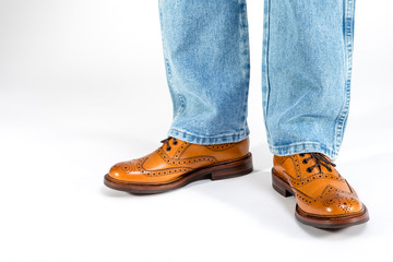 Closeup of Mens Legs on Brown Oxfords Brogues Shoes. Posing in Blue Jeans Against White Background