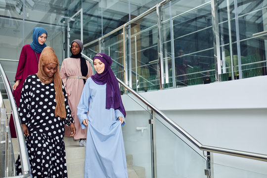 Multicultural group of female Arabian students, dressed in national dresses and scarfs going down the stairs of university, sharing ideas with each other on the way - Powered by Adobe