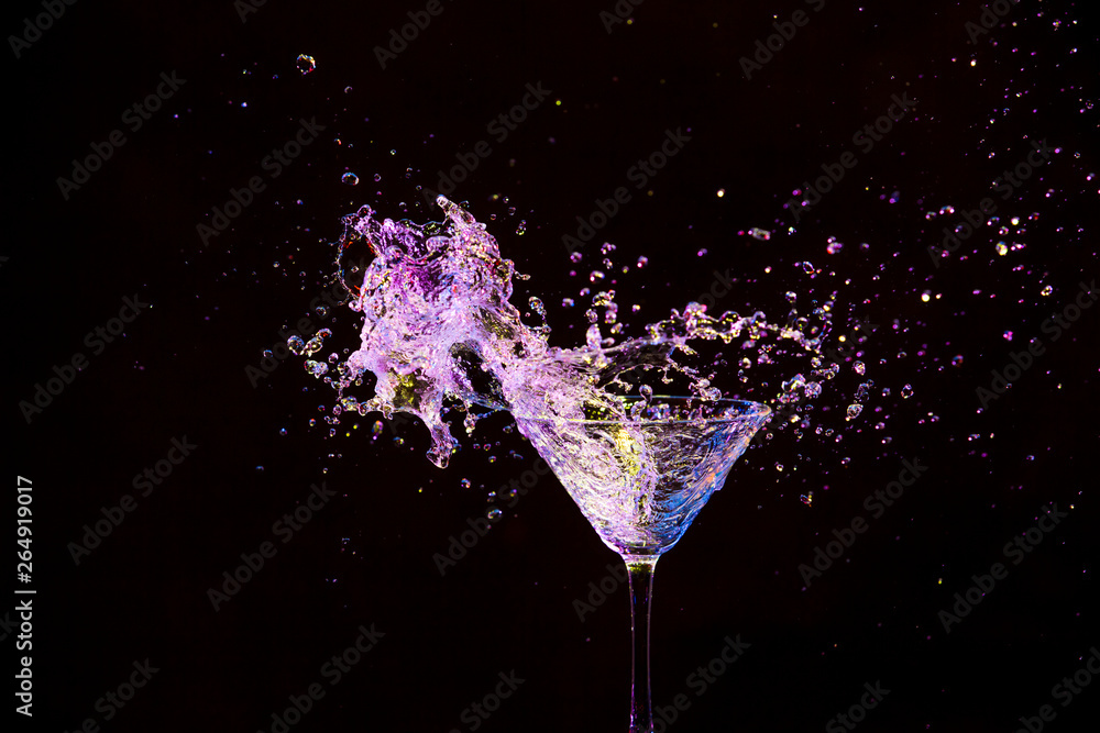 Wall mural high speed splash photography. burst of colorful liquid in wine glass. isolated over black.