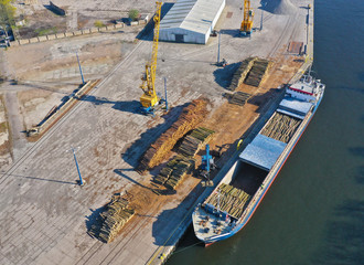 Aerial view on cargo ship in port bank loading wood stack on board using crane