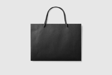 Mockup of a blank black paper shopping bag with handles on light grey background. High resolution.