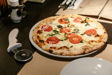 Hot Caprese Bianca Pizza from oven. Ingredients are Mozzarella, Parmesan, Olive oil, sliced tomato and Dough. Served on the table with Pizza Cutter.