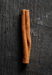 Single dried cinnamon stick on black wooden table - flat lay top view
