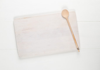 Empty white cutting board with wooden cooking spoon on white wooden table background