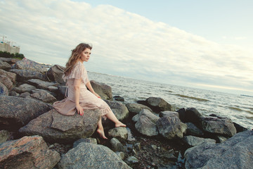 Pretty woman in boho dress on ocean coast against sky cloud background